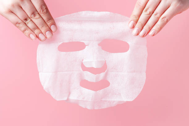 istock Female hands hold white fabric mask on pink background. 1219290022