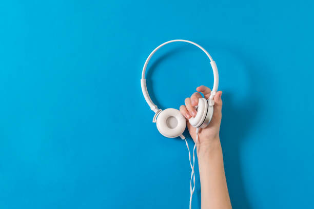 istock Hand holding white headphones with a wire on a bright blue background. 1219290143