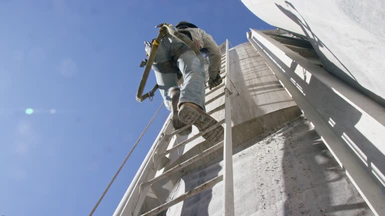 An Oilfield Worker Climbs a Ladder on the Side of a Mud Tank at an Oil and Gas Drilling Pad Site on a Sunny Morning