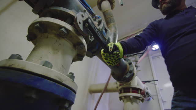 A Male Oilfield Worker in His Forties Opens/Closes Valves to Change the Pressure of Mud Flow in a Pump Room at an Oil and Gas Drilling Pad Site