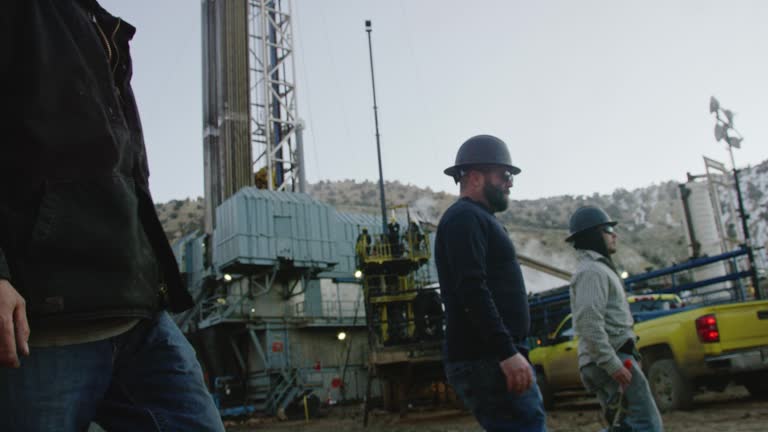 Slow Motion Shot of Several Male Oilfield Workers Walking through an Oil and Gas Drilling Pad Site on a Cold, Winter Morning