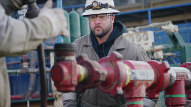 Slow Motion Shot of Two Male Oilfield Workers Pumping Down Lines at an Oil and Gas Drilling Pad Site on a Cold, Winter Morning
