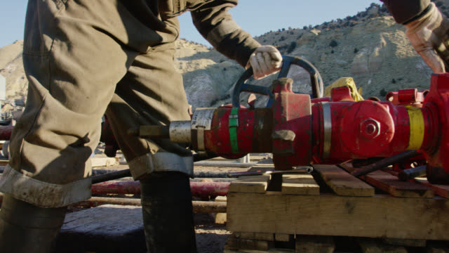 Slow Motion Shot of an Oilfield Worker in His Thirties Pumping Down Lines and Hitting a Pipe with a Hammer at an Oil and Gas Drilling Pad Site on a Cold, Sunny, Winter Morning