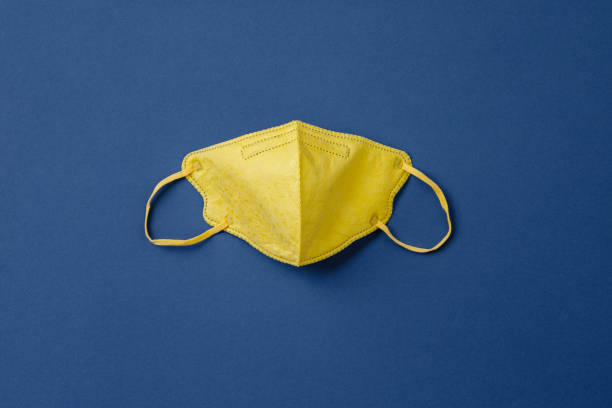 Yellow medical mask on blue paper background flat lay Yellow medical mask on blue paper background flat lay. Face mask protection against pollution, virus, flu and coronavirus. Health care and surgical concept. earth first aid stock pictures, royalty-free photos & images
