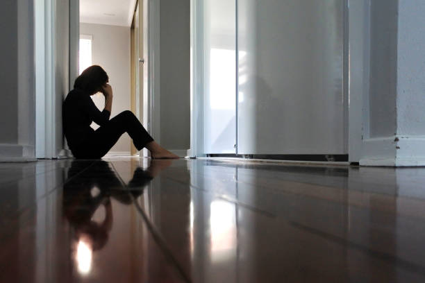 mujer triste sentada en el suelo oscuro del pasillo de la casa. - bad conditions fotografías e imágenes de stock
