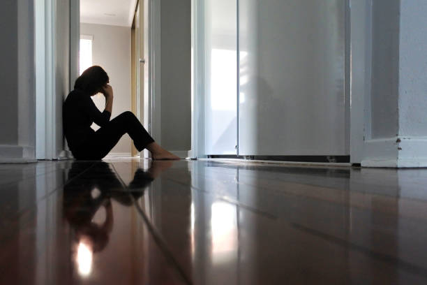 femme triste s’asseyant sur le plancher foncé de couloir de maison. - être seul photos et images de collection