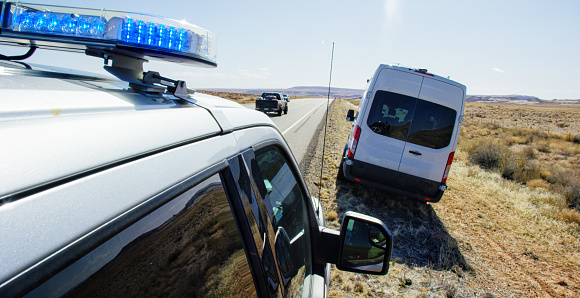 A Police Vehicle with Its Lights Pulls over a Large, White Van on the Side of the Highway/Interstate in the Deserts of Utah on a Bright, Sunny Day