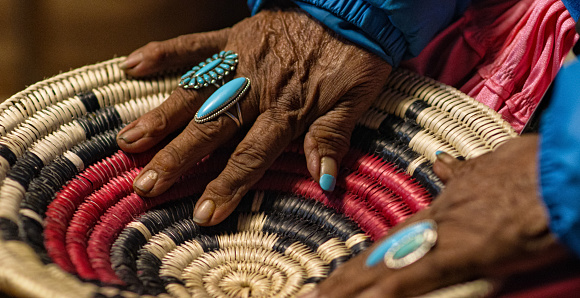 Una anciana mujer nativa americana (Navajo) que lleva anillos de color turquesa en sus dedos toca una cesta de navajo tejida photo