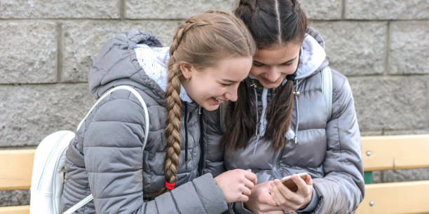 istock girlfriends with smartphone in their hands are sitting on bench 1219299069
