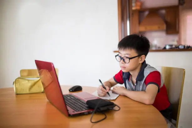 A student learning by doing schoolwork at home using a computer e-classes during COVID-19 pandemic. Distance learning online education or stay at home.