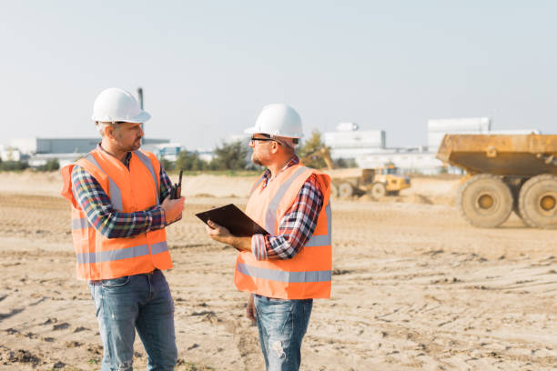istock Two builders in orange vests and helmets working on the road construction field 1219301785