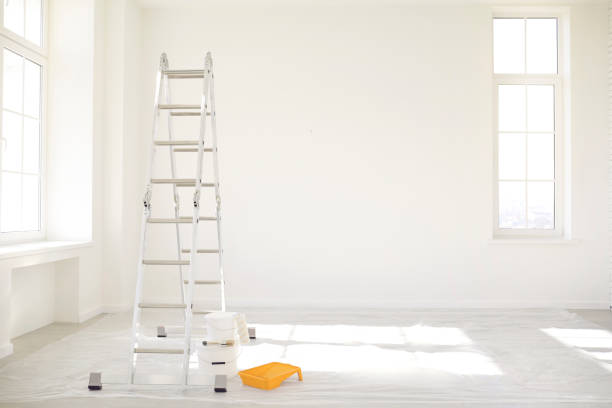 Painting in a white room with windows with a stepladder and paints on the floor.