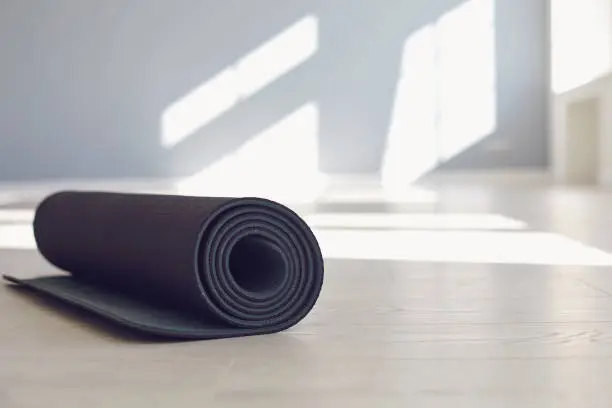 Black yoga mat on the floor of a bright sunny studio. The concept of an active lifestyle of sports life sports fitness yoga pilates meditation relaxation relaxation gym.