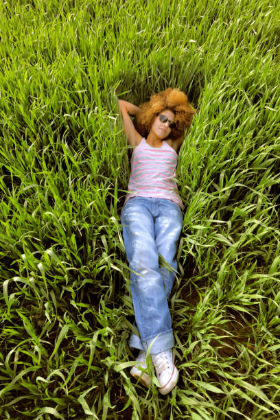 A young woman takes time out to relax in a\nfield. She is seen lying in the tall grass with \na trendy pair of sunglasses on.