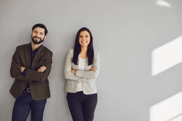 Photo of A businessman and a business woman are standing against a gray wall