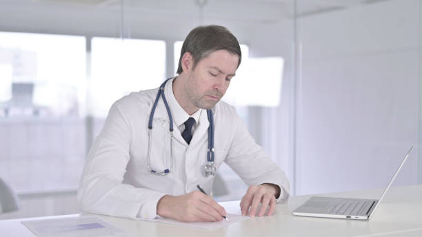 istock Serious Middle Aged Doctor doing Paperwork in Clinic 1219305156