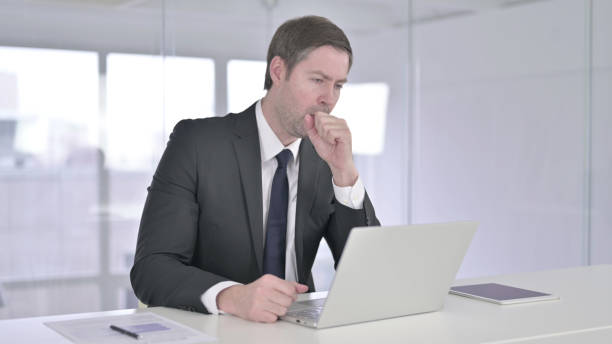 istock Coughing Middle Aged Businessman Working on Laptop 1219305734