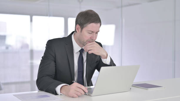 istock Middle Aged Businessman Thinking and Working on Laptop 1219306272