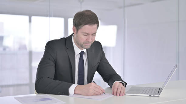 istock Serious Middle Aged Businessman doing Paperwork in Office 1219306430