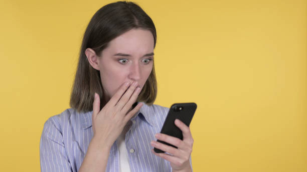 istock Shocked Young Woman Using Smartphone, Yellow Background 1219306523