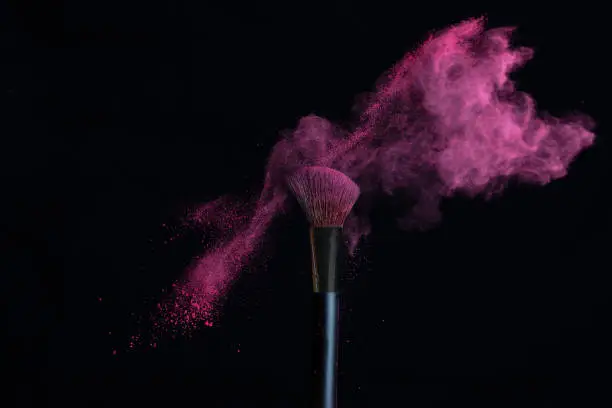 Make-up brush with pink powder explosion isolated in a black background