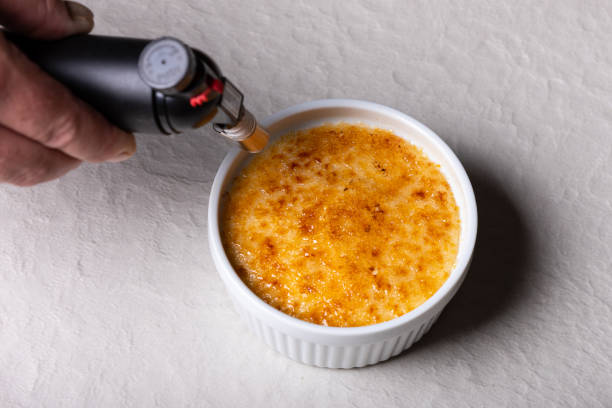 Chef making a crème brulee in a small white bowl with a torch flame stock photo