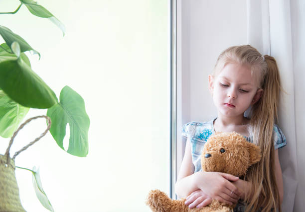 istock Sad child girl by the window 1219309663