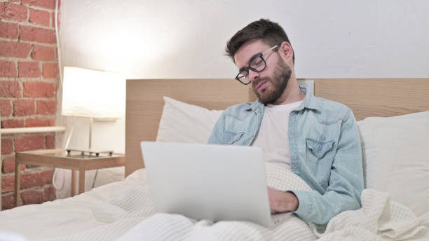 young man in glasses working on laptop and taking nap in bed - 15851 imagens e fotografias de stock