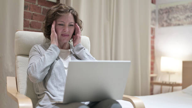 istock Old Woman with Headache Using Laptop on Chair 1219309758