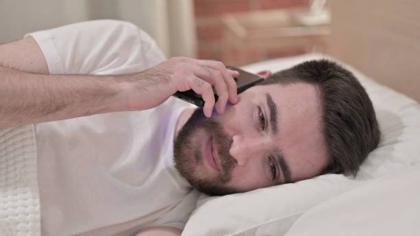 istock Young Man Talking on Smartphone in Bed 1219310349