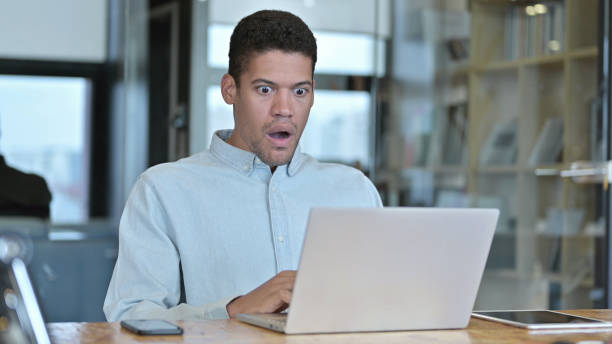 istock Young African Man  getting Shock on Laptop at Work 1219310887