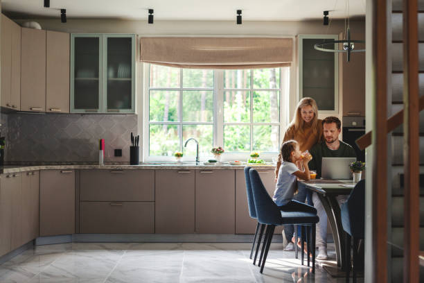 istock Middle aged man working on laptop computer in domestic kitchen surrounded by cute little daughter drinking juice and beautiful loving wife 1219316862