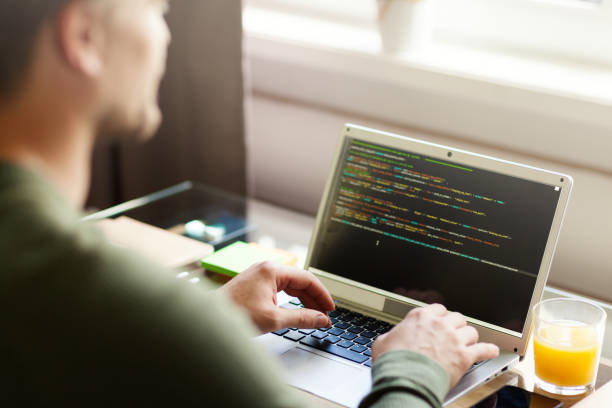 istock Over the shoulder view of defocused man coding on laptop computer sitting at desk at home 1219316882