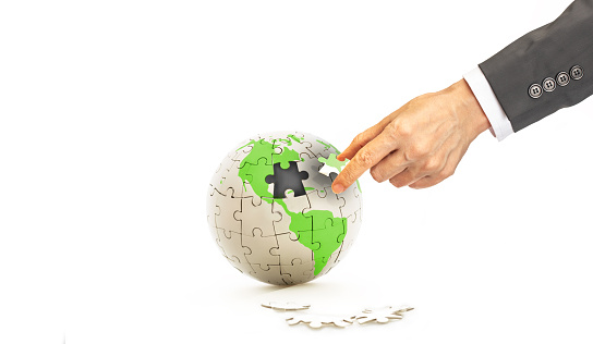 Create your own way concept, Earth jigsaw puzzle with green world map missing one piece of jigsaw and businessman hand holding the missing piece of jigsaw on white background
