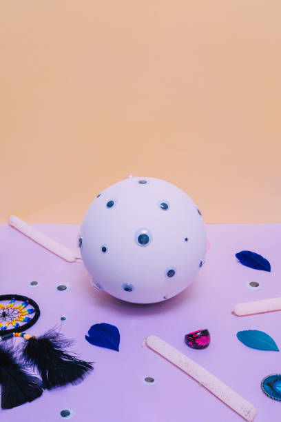 istock A white fortune telling ball with many eyes, a dream catcher, glittering candles, a ring and feathers on a light purple or lilac and yellow background. Modern abstract minimal pop art. 1219325047