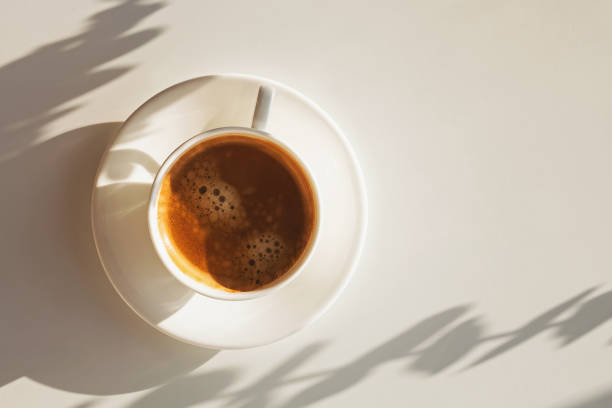 istock Cup of coffee atanding on the white table in sunlight dropping shadow 1219333085