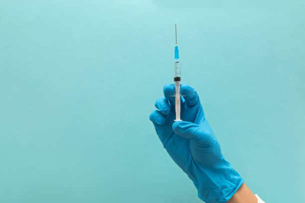 istock Hand in blue gloves holding syringe isolated on blue background 1219333781