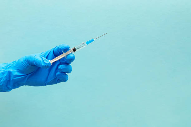 istock Hand in blue gloves holding syringe isolated on blue background. 1219333807