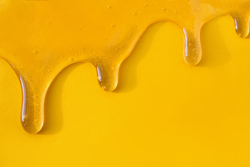 Flow of sweet honey on the yellow background with copy space