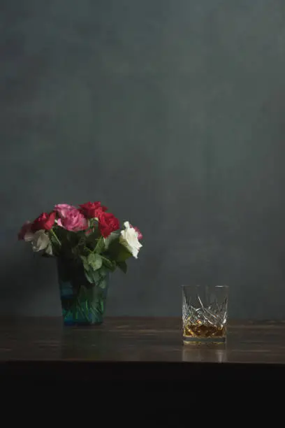 Photo of Glass of whiskey and roses on a wooden table.