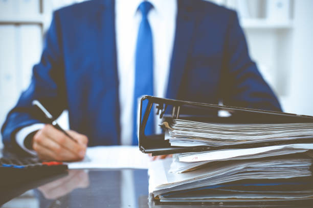 istock Binders with papers waiting to be processed with businessman or bookkeeper back in blur. Accounting planning budget. Audit, insurance and business concept 1219336953