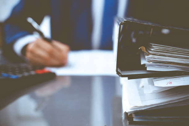 istock Binders with papers waiting to be processed with businessman or bookkeeper back in blur. Accounting planning budget. Audit, insurance and business concept 1219336957