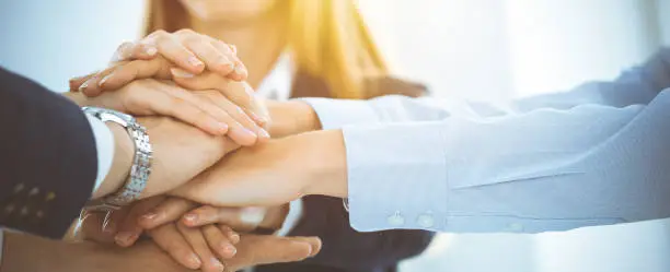 Photo of Business team showing unity with their hands together in sunny office. Group of people joining hands and representing concept of friendship, teamwork and partnership