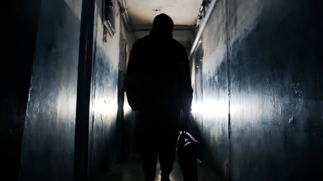 Silhouette of Unrecognizable Criminal Man Wearing Black Jacket and Carrying a Bag in Long Dark Hallway.