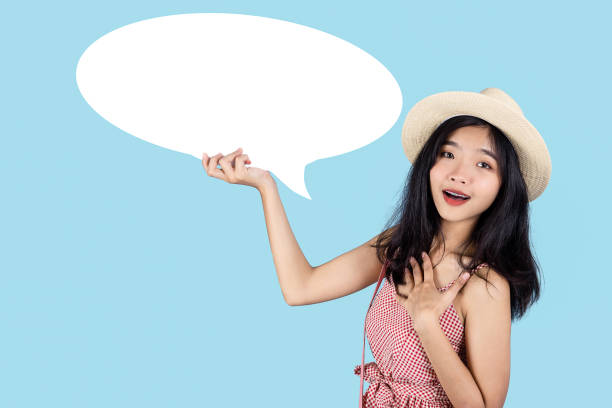 istock Smiling Asian tourist holding white speech bubble on blue background. 1219342562