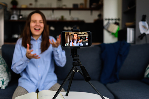 Smiling Woman in shirt Recording video at home for her video blog. Using smartphone