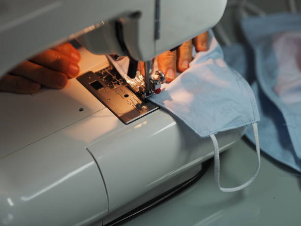 女性は、ほこりpm 2.5、コロナウイルス流行、自宅で作られたdiyでウイルスcovid-19作業の間に保護された顔の医療マスクを縫うために縫製機を使用します - thread tailor art sewing ストックフォトと画像