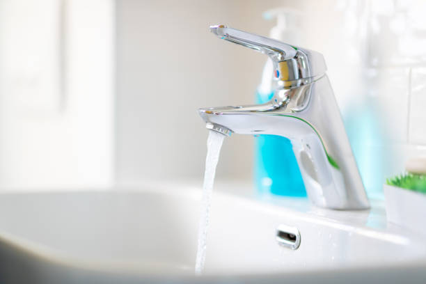 Water running from the tap in bathroom sink with hand sanitizer dispenser