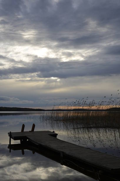 istock A dark pier on the waterside. Mirror water surface reflecting sunlit clouds. 1219349204