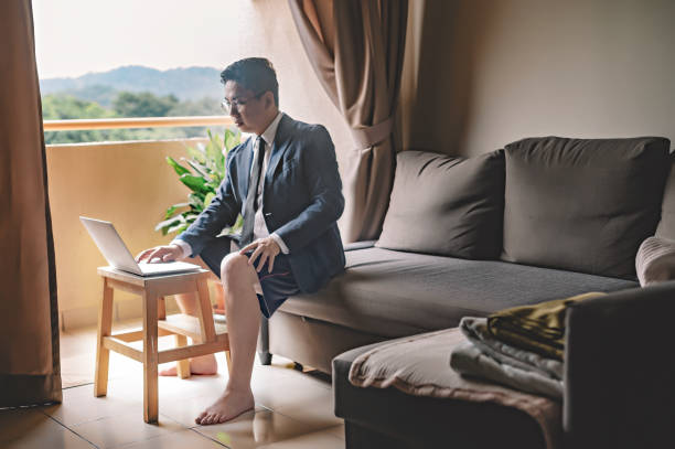 ネクタイとスーツと短いパンツを持つアジアの中国人の中年男性は、彼のビジネスパートナーと同僚の仮想ビジネスミーティングのための彼のリビングルームでラップトップを使用してソフ� - blazer men suit business ストックフォトと画像